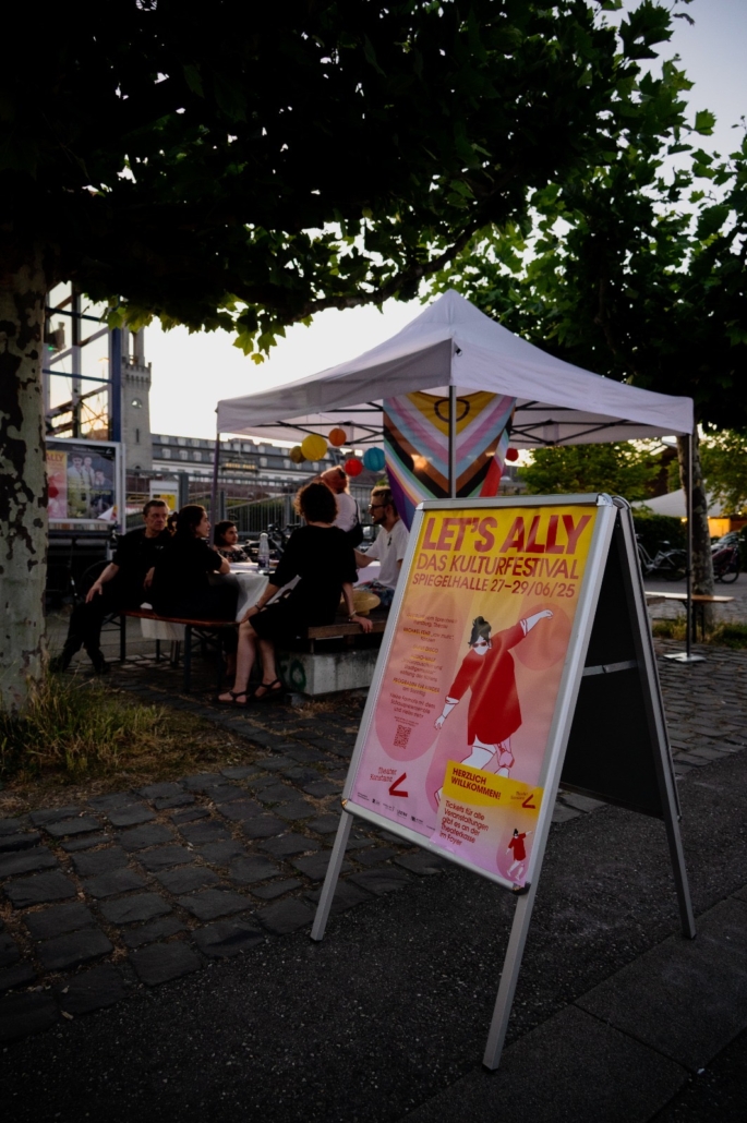 Buntes Programmplakat vor einem Pavillion am Eingang zum "Lets ally"-Festival in Konstanz