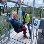 Ein Mitarbeiter des Ausflugsziels "Waldflug" in Schömberg trägt ein hellgrünes T-Shirt und schnallt Rika auf einer Aussichtsplattform in einem Sitz der Attraktion "Flyline" an.