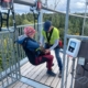 Ein Mitarbeiter des Ausflugsziels "Waldflug" in Schömberg trägt ein hellgrünes T-Shirt und schnallt Rika auf einer Aussichtsplattform in einem Sitz der Attraktion "Flyline" an.