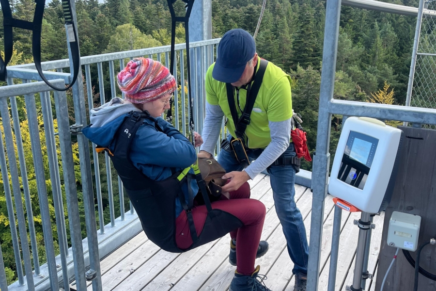Ein Mitarbeiter des Ausflugsziels "Waldflug" in Schömberg trägt ein hellgrünes T-Shirt und schnallt Rika auf einer Aussichtsplattform in einem Sitz der Attraktion "Flyline" an.